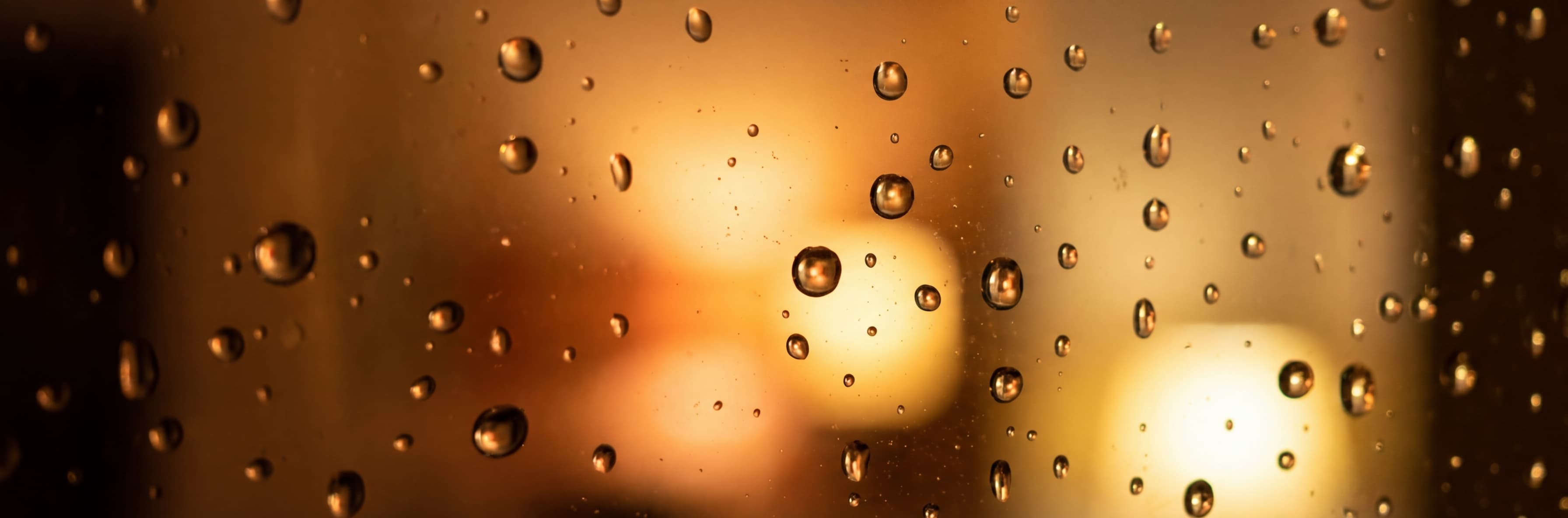 Rain droplets on a window with warm light glowing through